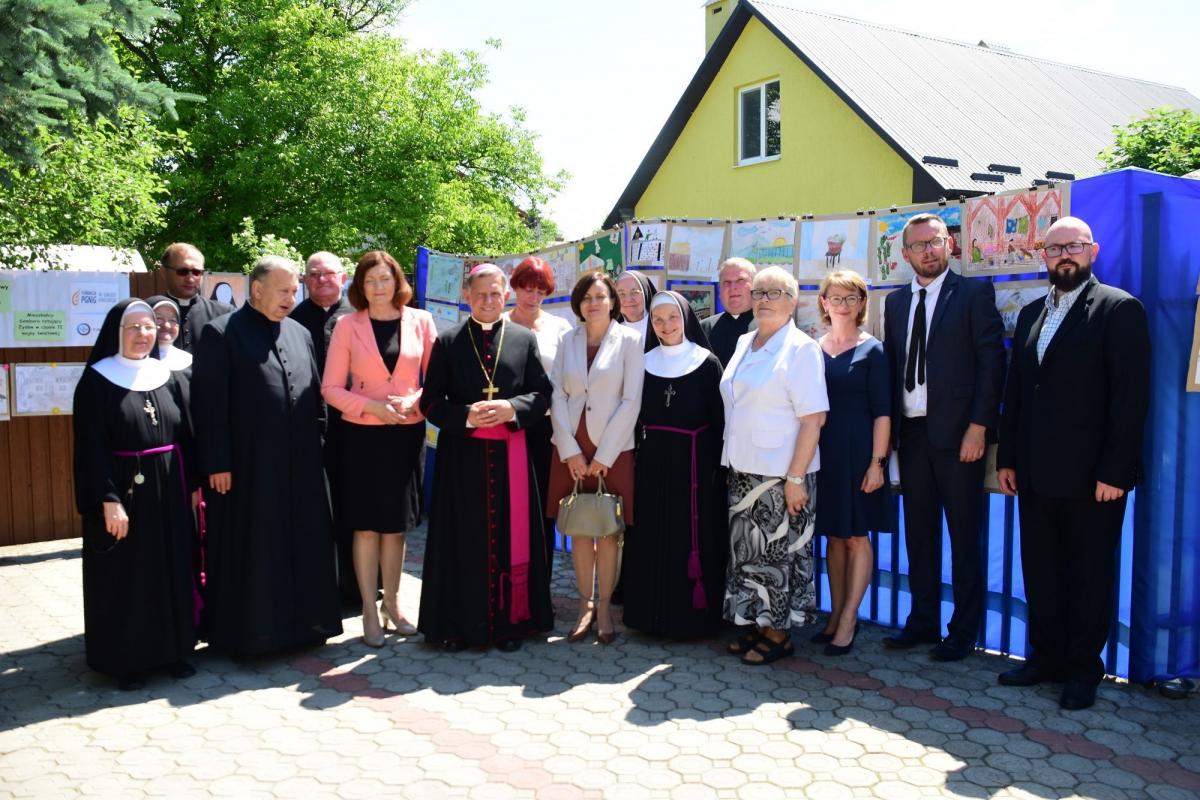 Pamiątkowe zdjęcie zaproszonych gości na tle prac dzieci. W środku abp M. Mokrzycki, prof. E. Rączy i s. E. Ślemp.  