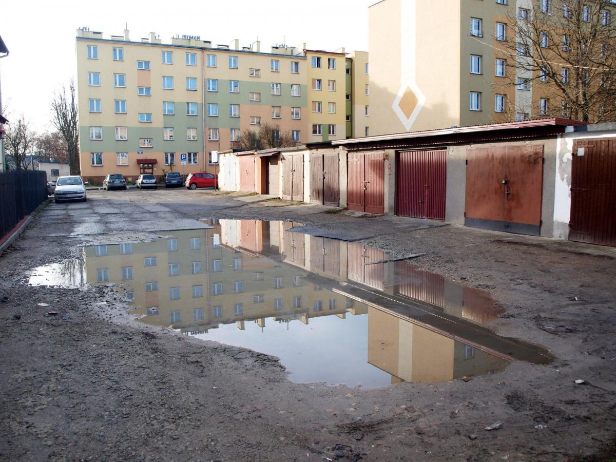 Nawierzchnia „parkingu” to uszkodzona, ukruszona trylinka oraz będące w podobnym stanie płyty betonowe, ciągnące się wzdłuż szeregu garaży. Kiedy popada deszcz, trwałym elementem krajobrazu, tuż obok garaży, jest potężna kałuża.<br/>fot.Mariusz Godos
