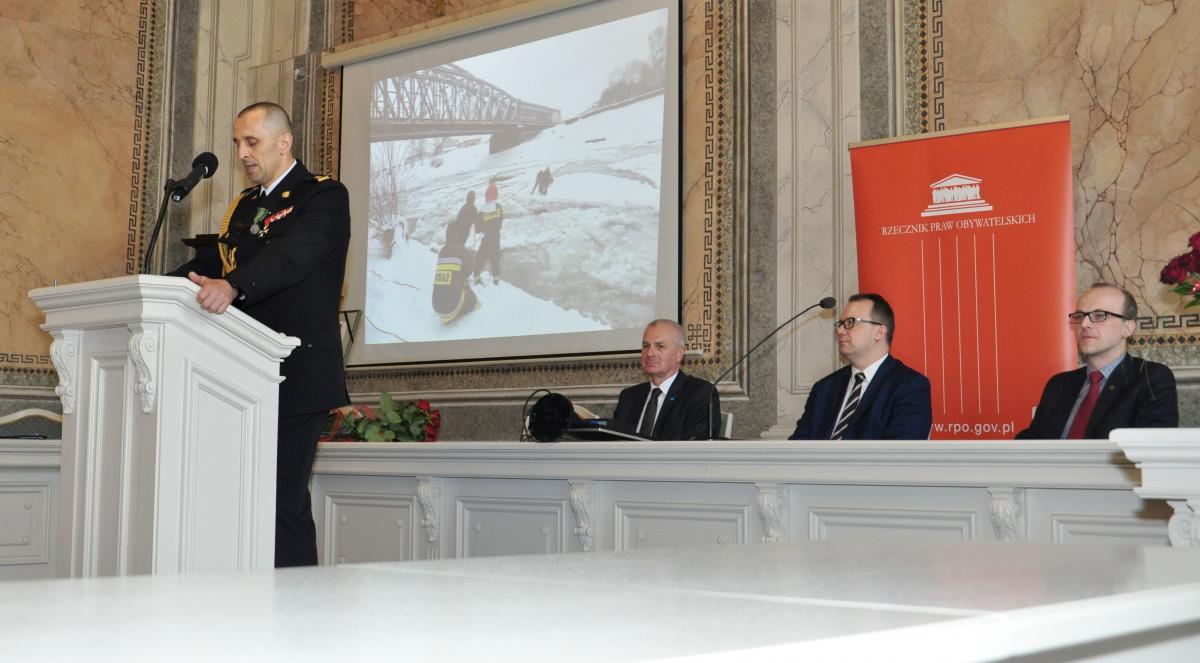 Brygadier Daniel Dryniak na mównicy. Przy stole prezydialnym od prawej: przemyślanin, sędzia Trybunału Konstytucyjnego prof. Marek Zubik,  Rzecznik Praw Obywatelskich dr Adam Bodnar oraz prezydent Przemyśla Robert Choma.<br/>fot.Agata Czereba / UM Przemyśl