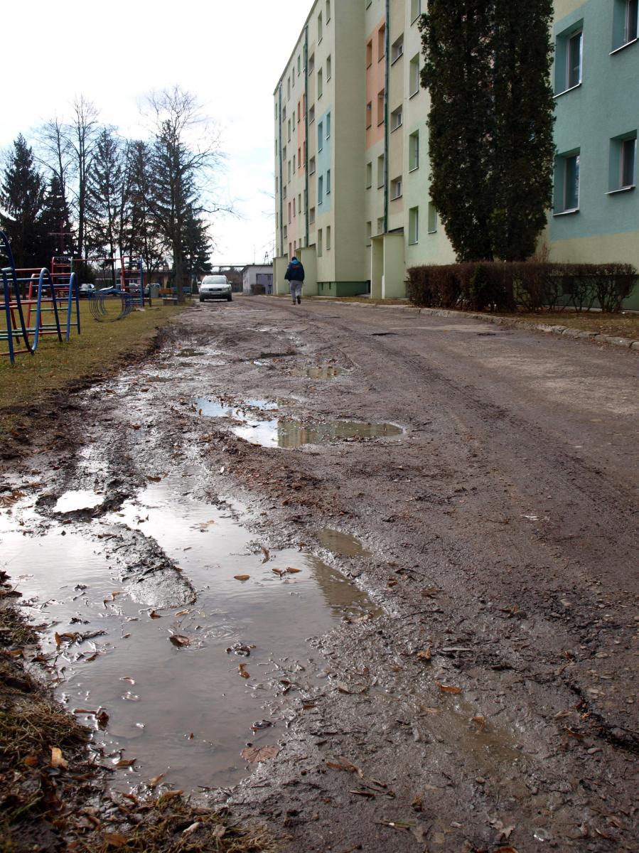 Teren przed wejściami do czterech klatek schodowych bloku przy ul. Ofiar Katynia 12A wygląda fatalnie. Rozkruszony asfalt, głębokie dziury w nawierzchni, grzęzawisko w pobliżu – . o to mają pretensje lokatorzy.<br/>fot.Mariusz Godos