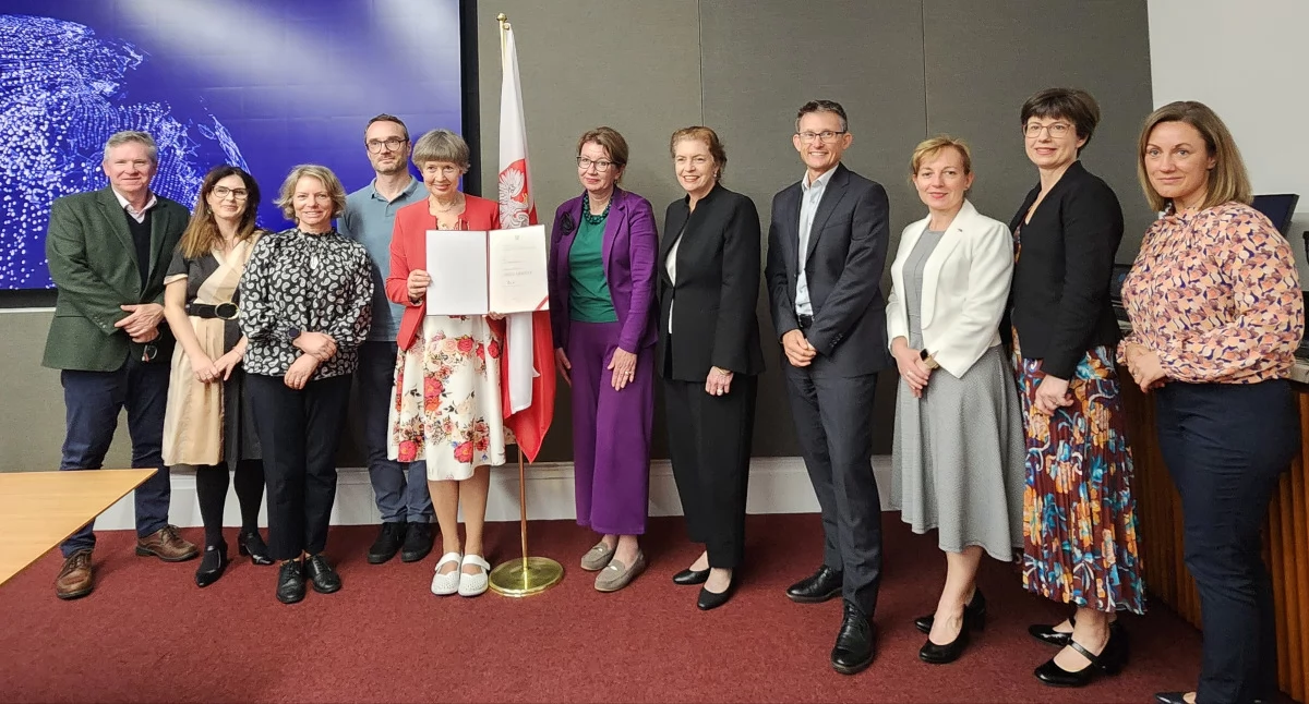 Na zdjęciu prof. Lidia Morawska prezentuje wyjątkowe wyróżnienie doceniające jej wkład w promocję Polski za granicą. Obok (w fioletowym) Karolina Cemka – szefowa Chargée d’Affaires a.i. Rzeczypospolitej Polskiej w Australii./Fot. zbiory prywatne L.Morawskiej